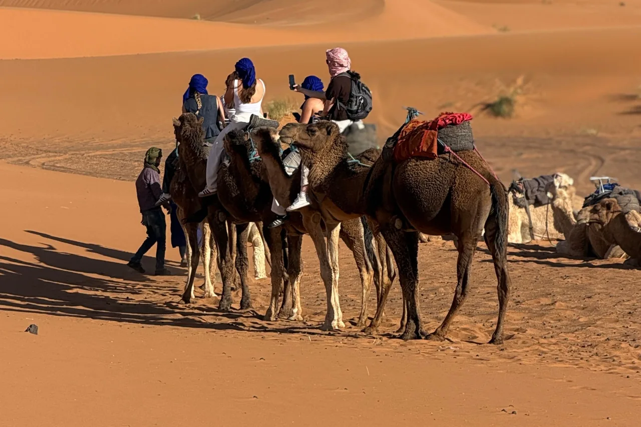 Camel riders crossing sunlit sand dunes