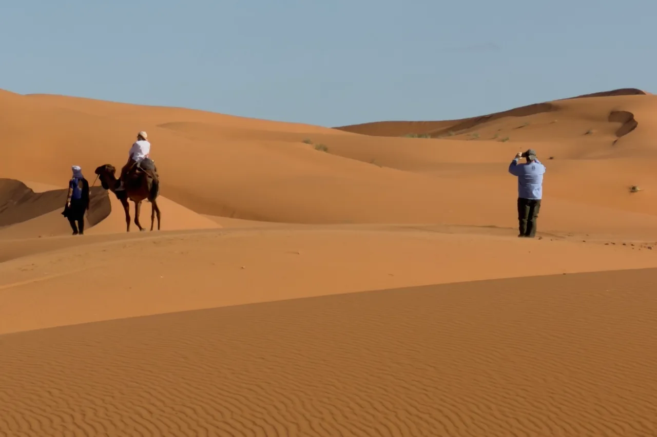 Travelers walking across sunlit sand dunes