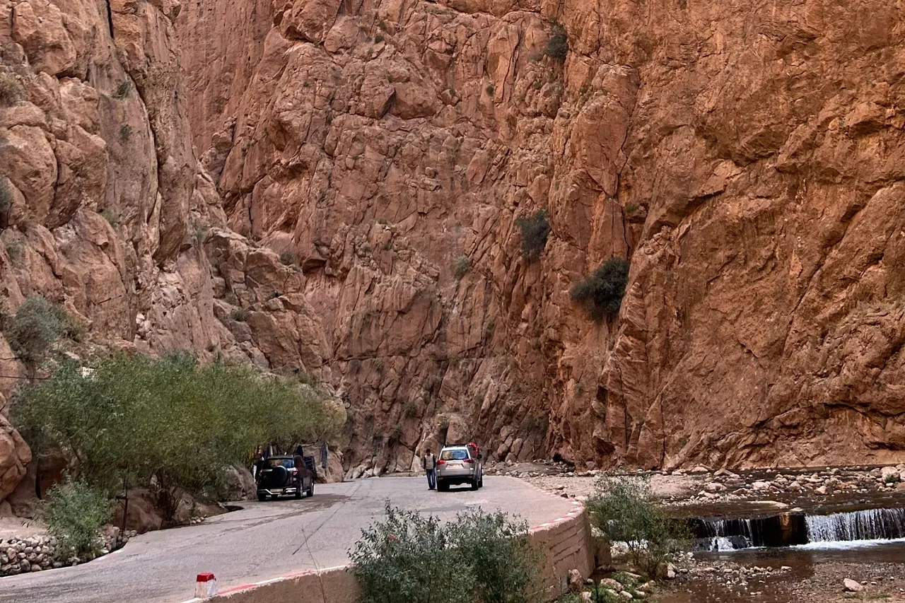 A winding road and stream between steep rocky gorge walls